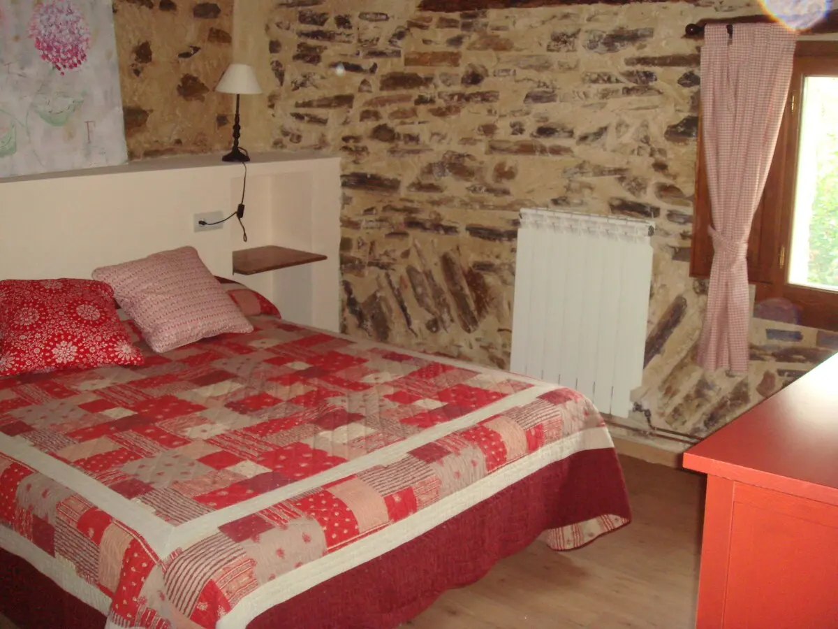 Dormitorio de matrimonio con colcha roja y pared de piedra